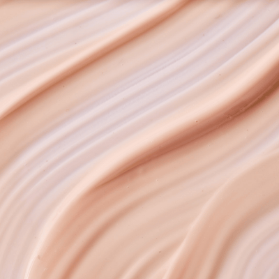 Gros plan sur la texture d’une crème beige clair, lisse et légère, aux ondulations douces et au fini brillant.